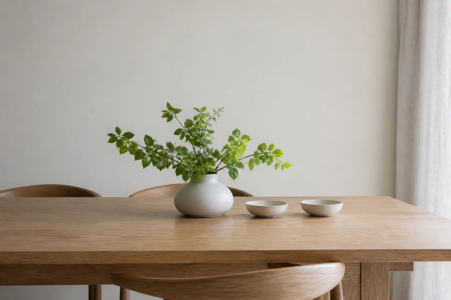 A cleared white oak dining table in morning light with a low vase of greenery
